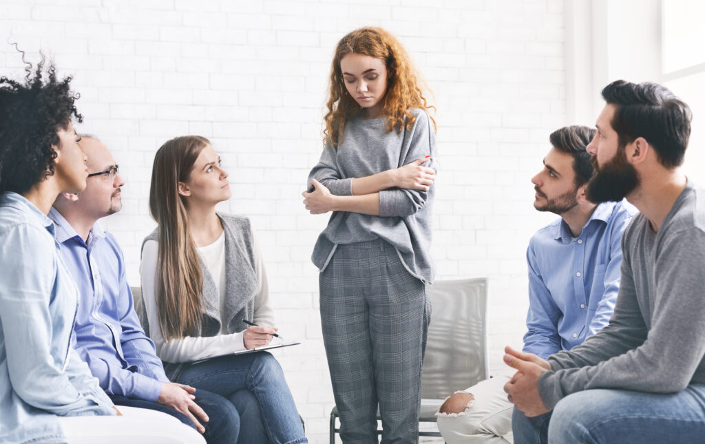 addicted woman talking talking during rehab group meeting